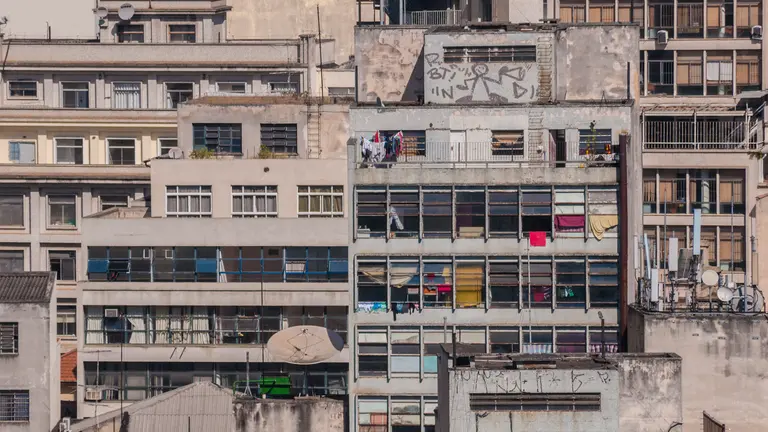 A close-up view of a building, with an abundance of windows, washing hanging from balconies and TV dishes shown outside the densely packed apartments.