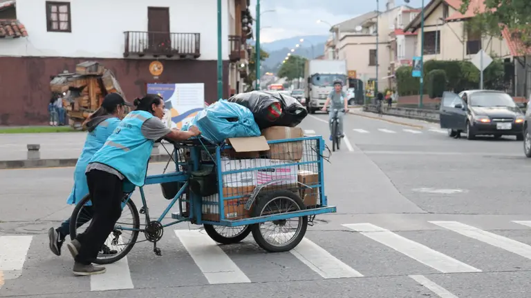 Two people pushing a cart carrying waste trhough a pedestrian crossing.