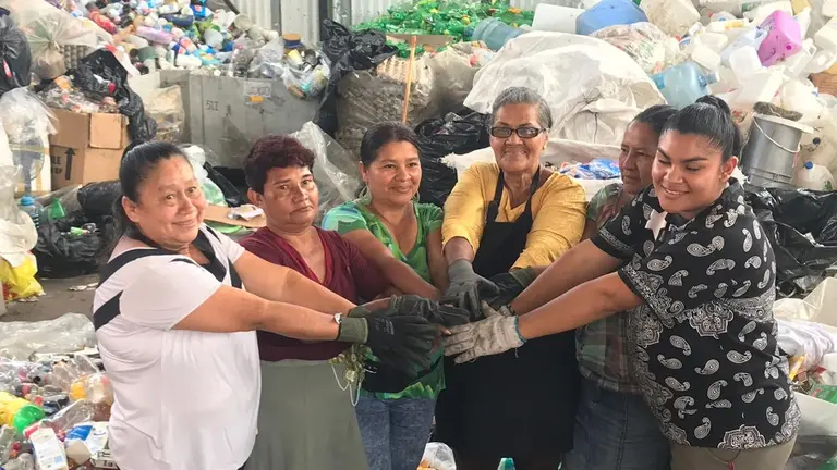 Group of women putting their hands together, surrounded by bags of garbage.