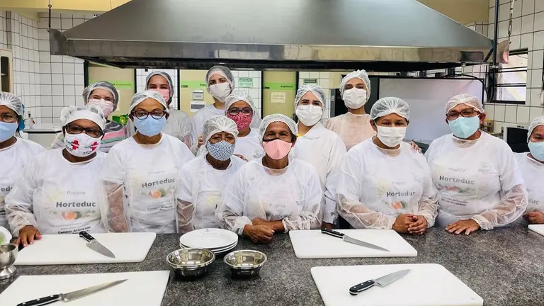A group of women in white uniforms standing in front of a kitchen.