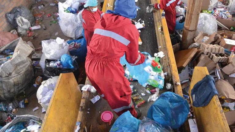 Workers in red overalls sorting through garbage to separate recyclable materials.