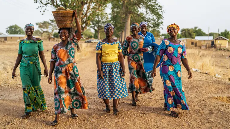 A group of smiling women, with trees in the background.