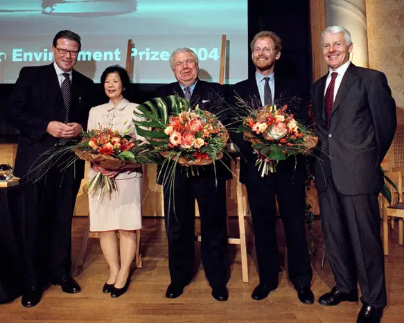 A group of people in business clothes. Three are holding bunches of flowers.