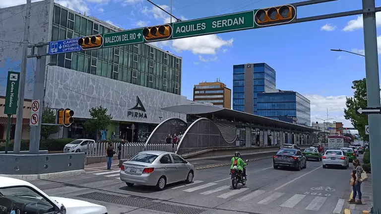 A woman waits beside a busy intersection as cars and motorbikes drive past. 