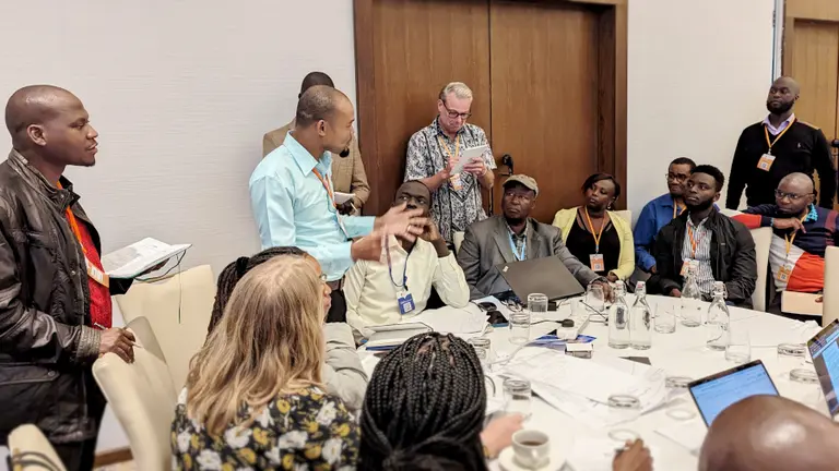 A man standing talking to a group people seated around a table.