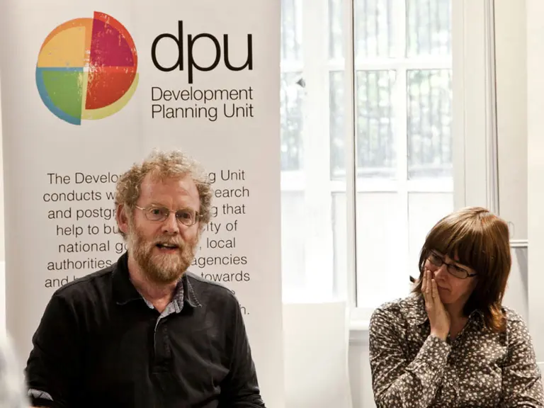 A man sits next to a woman in front of a sign branded "DPU"