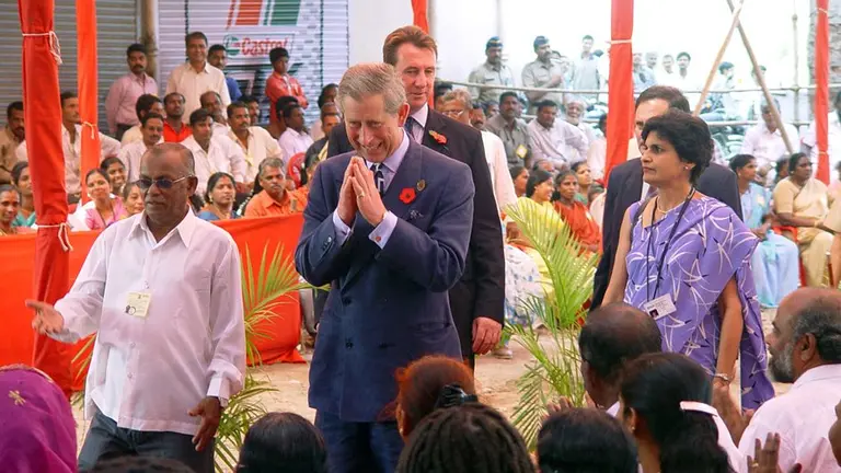 A man clasps his hands together in a praying gesture while being guided by another man.