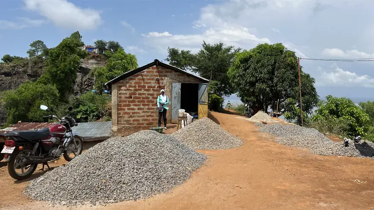 A small shed with piles of gravel and sand outside. On a motorbike, sheets of corrugated iron.
