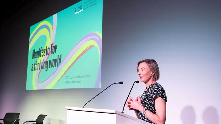 A woman stands at a podium giving a speech, while in the background is an image of a publication cover, saying: "Manifesto for a thriving world".