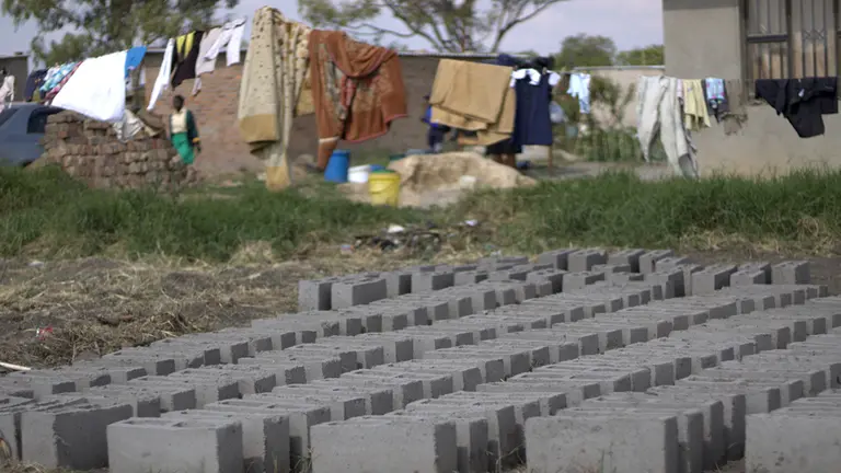 Rows of grey bricks on the ground outside a house. In the background, washing is hanging on a line.
