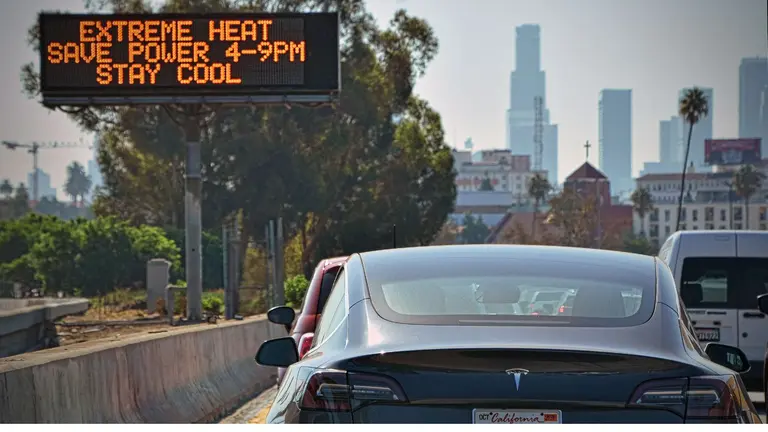 Cars stopped on the motorway. A digital sign reads "Extreme heat. Save power 4-9PM. Stay cool"