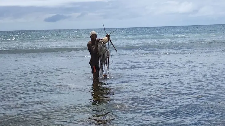 A fisherman, standing surrounded by water, holds up an octopus he has caught.