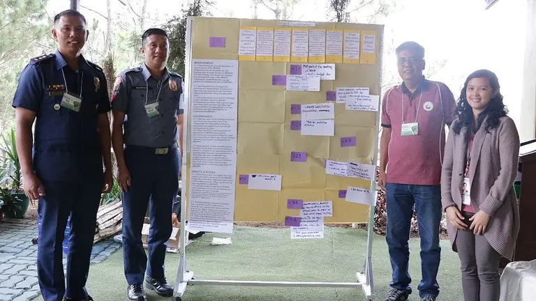 Three men and a woman stand either side of a presentation board facing the camera.