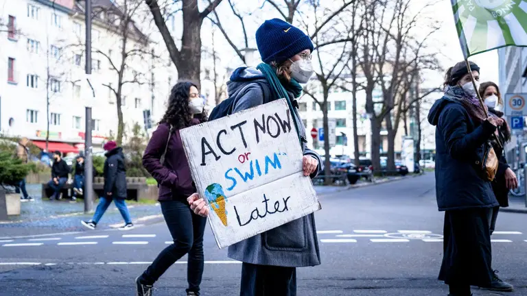 Climate protestor holding sign that reads "Act now or swim later"