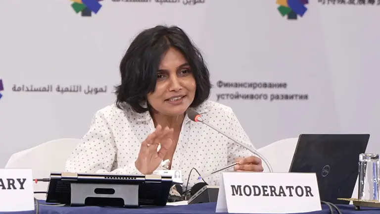 A woman, seated behind a sign saying 'moderator' speaks into a microphone at a conference.