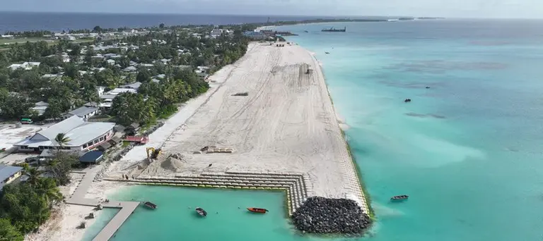 An aerial view of a small harbour/coastal defence project showing land to the left, and sea to the right.