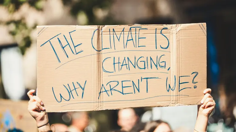 Person hold up sign saying 'The climate is changing, why aren't we?'.