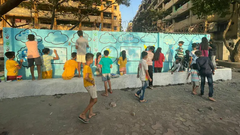 A group of lively young children enthusiastically paint a previously grim looking wall in bright colours.