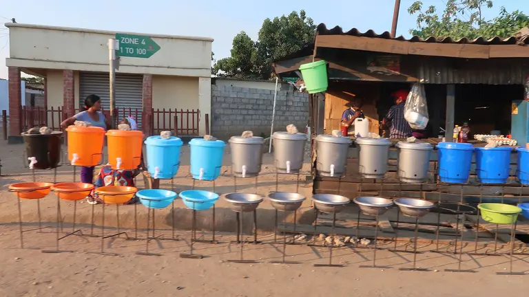A row of multicoloured containers filled with water beside a dusty road. 