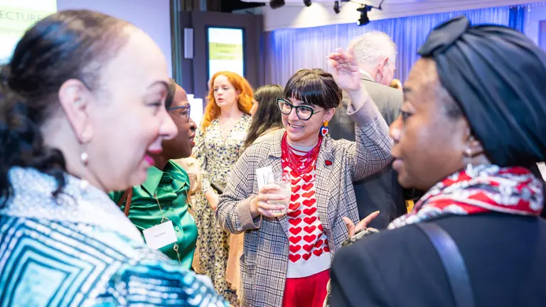 Several women of colour smile as they chat to one another in a social gathering.