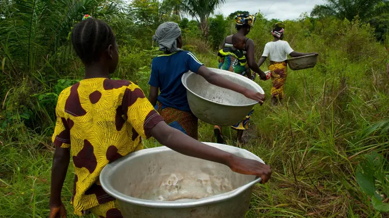 Group of four women carrying big basins on the way to get clean water. They are wearing colorful clothing.