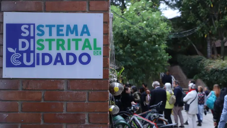 Image of sing on building, with people seen on the background. Sign reads 'Sistema Distrital de Cuidado'.
