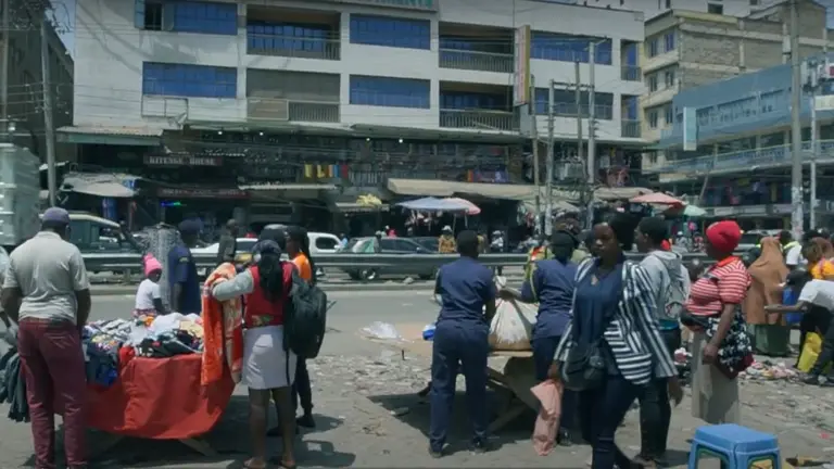 People on the busy street of Nairobi, selling goods on tables set at the edge of a road.