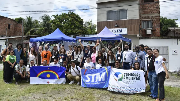 Group of people gathered for a group photo. They are holding a banner that reads 'Somos Todos Muribeca'.