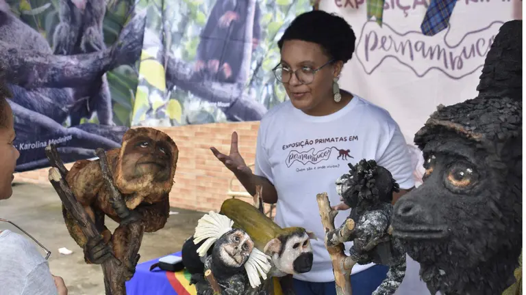 Two people in conversation at a stand with statues of different monkeys found in the forests of Brazil.
