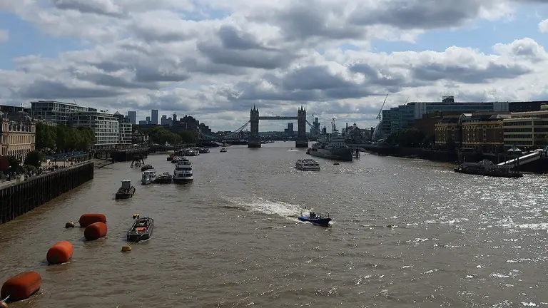 An aerial view of the River Thames, with boats on the water and a bridge in the background.  