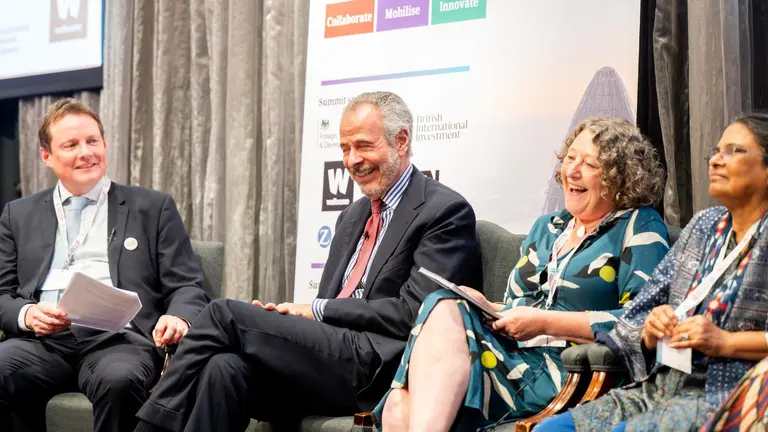 Panel members sitting on a stage with a banner behind, laughing a talking.