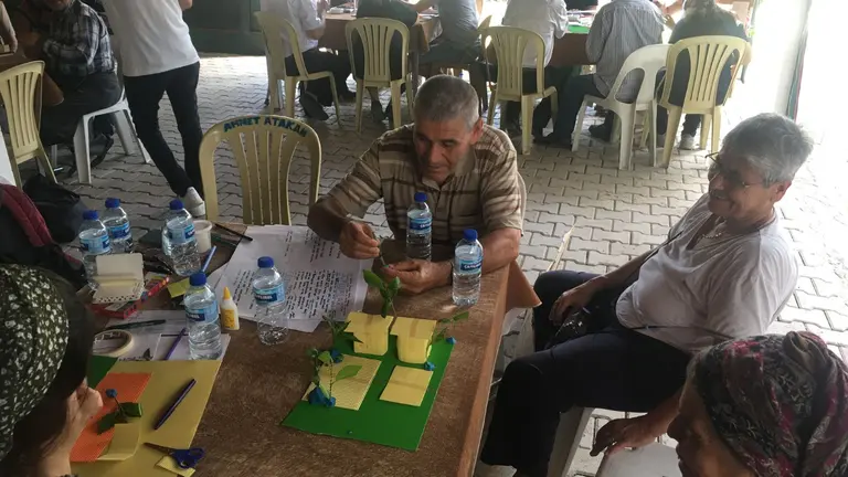 People sitting around a table, discussing and building model houses out of colorful paper materials and glue.