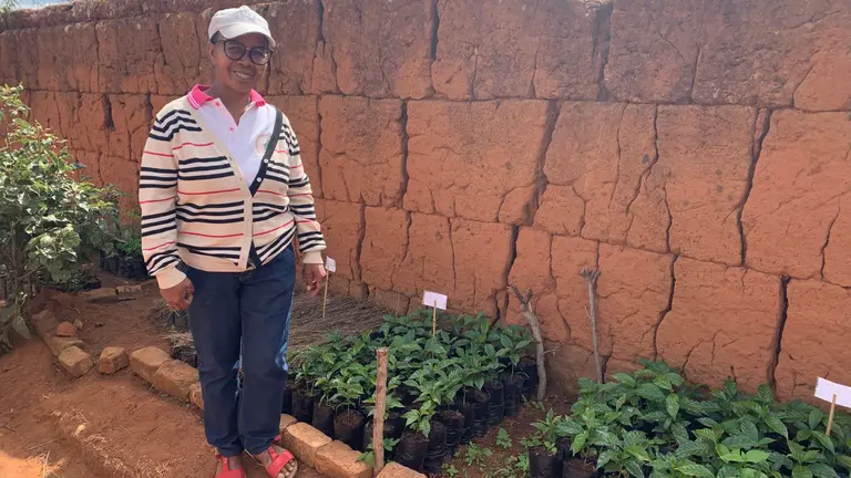 Woman standing next to tree and coffee seedlings, in a back garden.