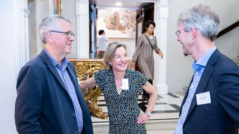 A woman smiles as she chats with two men either side of her at an event.