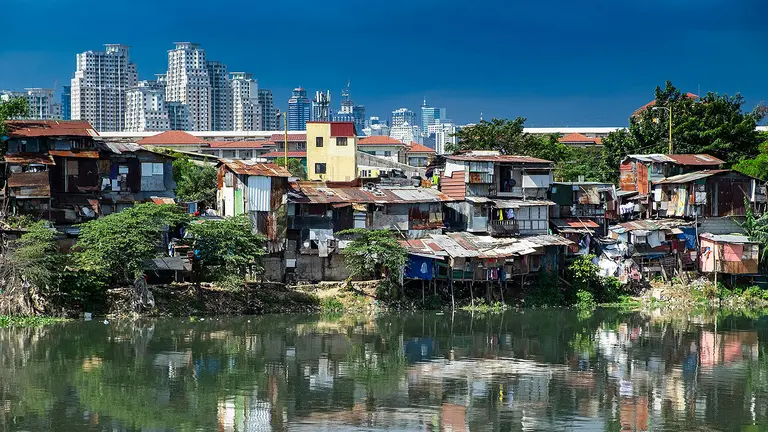 A horizon photo of a city, showing slums in the foreground conflicting with skyscrapers behind in the distance.
