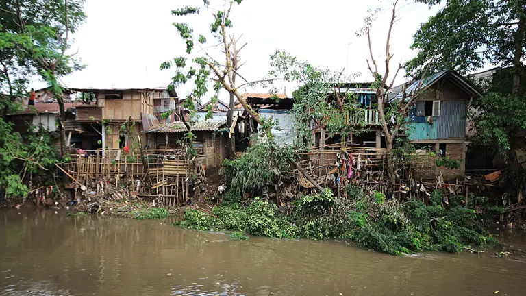 Informal settlement with torn-down houses on the edge of a body of water in Jakarta.