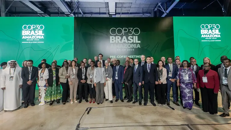 A large number of people stand and pose for a photo in front of a huge COP30 sign.