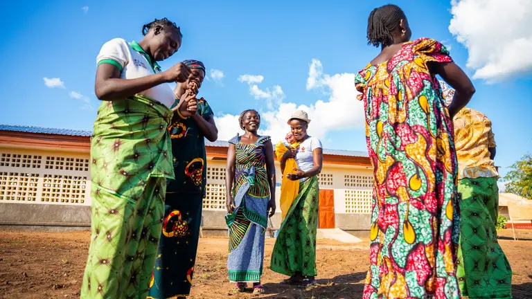 Group of local women from the Central African Republic gathered in a circle, speaking and laughing. They are wearing traditional dress.