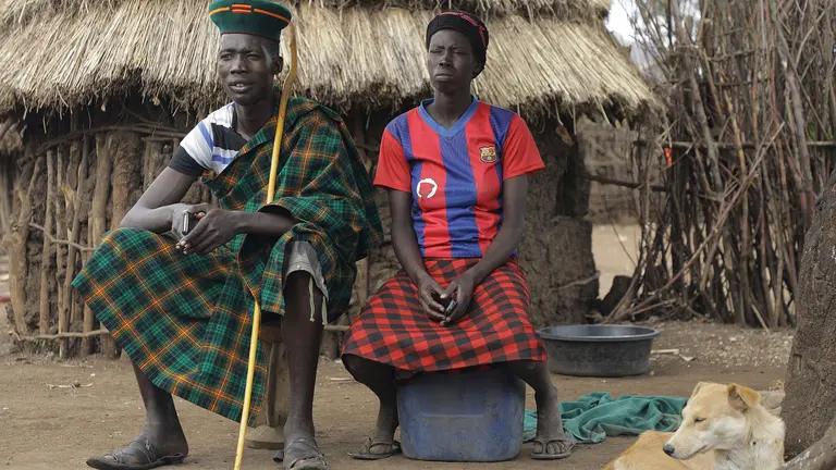 A man and woman sit beside one another outside in front of a traditional pastoralist hut as part of an interview.