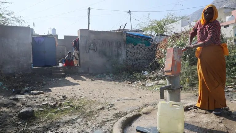 Woman pumping water into a plastic canister. She is wearing a traditional saree.