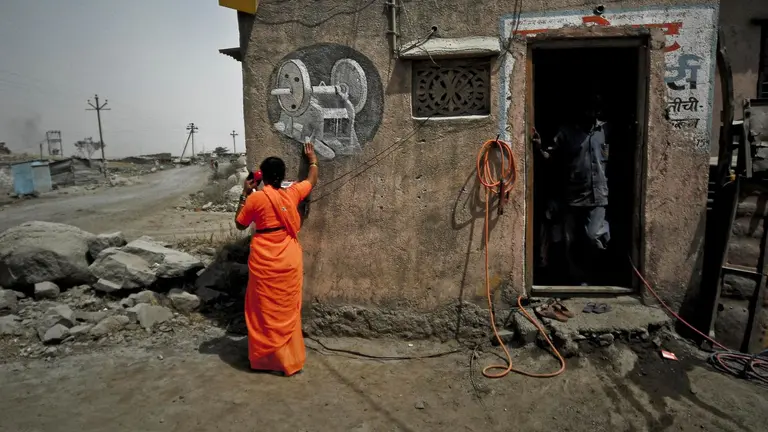 Woman worker in a stone quarry wearing a bright orange saree is making a phone call using a land line outside a building.