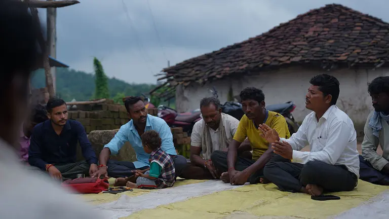A discussion takes place among a group of people seated on blankets outdoors.