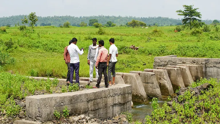 A group of people gather standing on a dam that looks in disrepair.