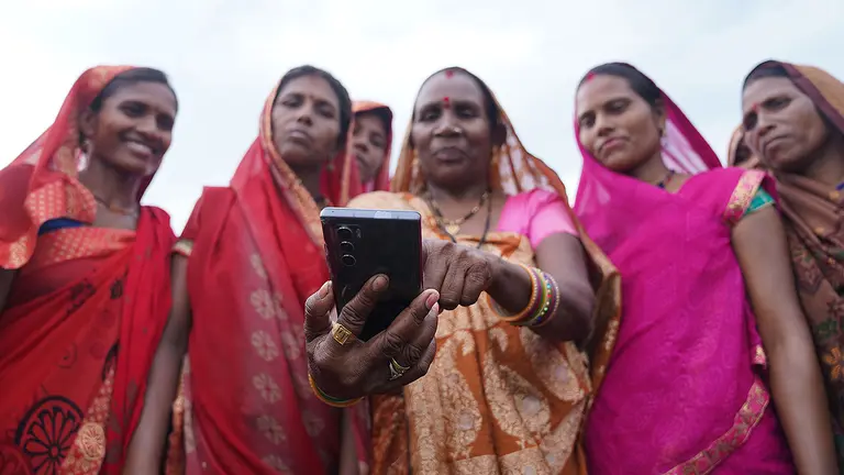 A group of five women look at mobile phone the middle woman is holding out in front of her.