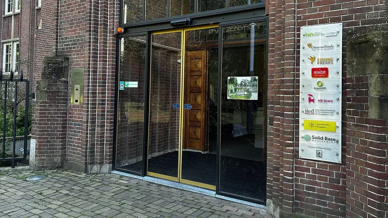 The front glass doors to an office building, with a name plate of business owners beside it on the wall.