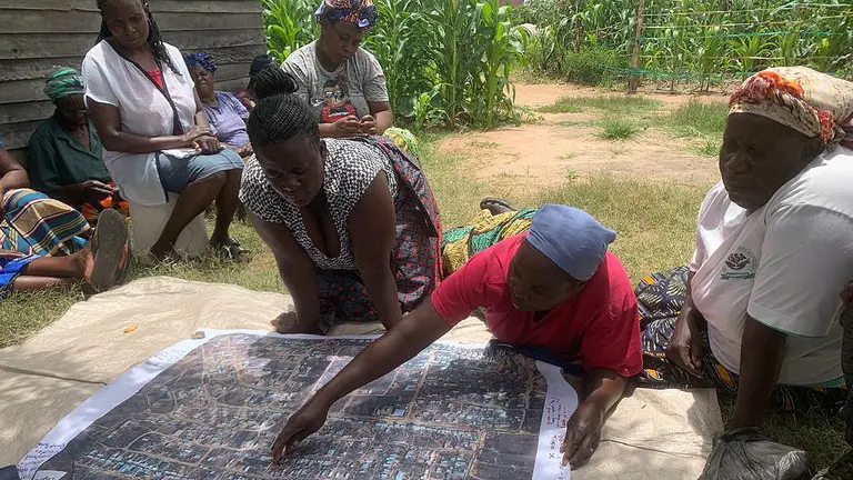 A group of women lean over a map laid out on grass outside.