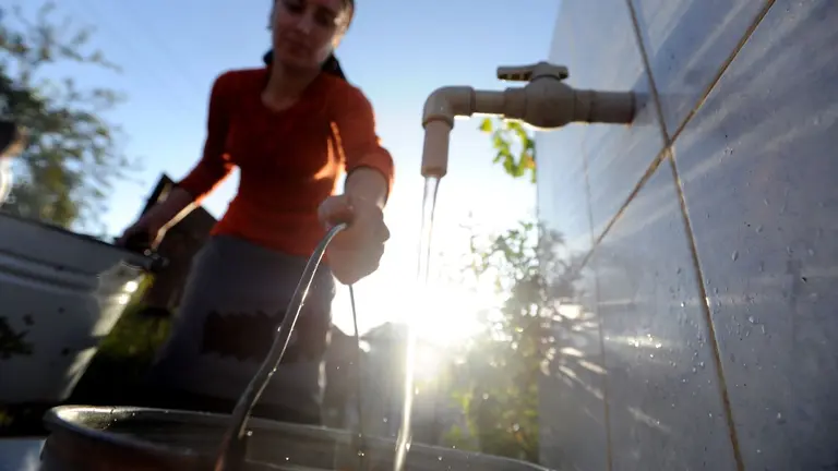 Woman is filling up bucket with drinking water from an outside tap.