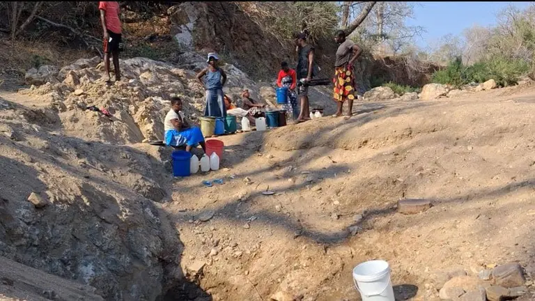 Women and girls collect water in buckets at a water source.