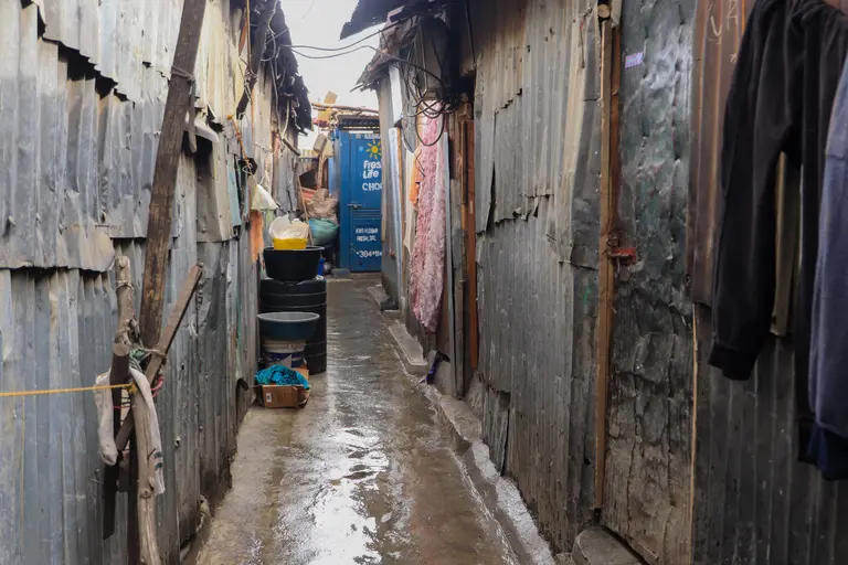 A narrow outdoor path between corrugated iron buildings either side with little space.