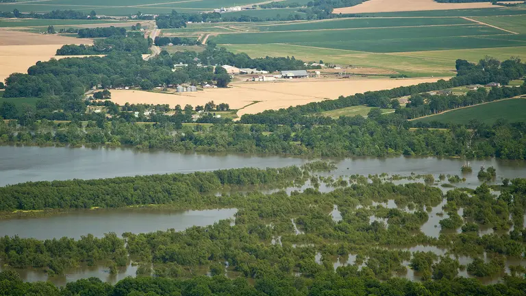 An aerial view of a river that has flooded the surrounding area, showing fields and houses partly submerged by water.